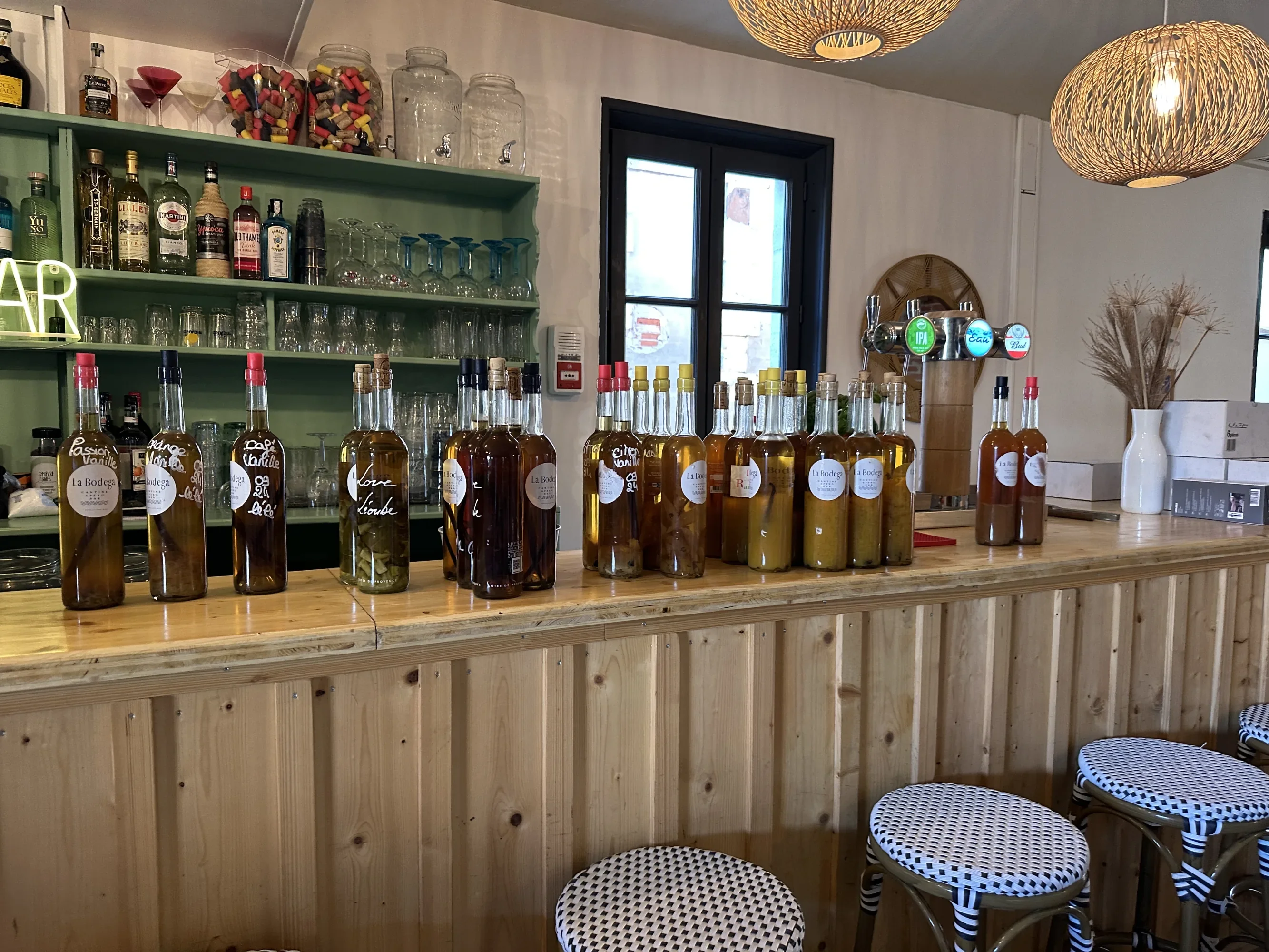 Le comptoir bois clair, bouteilles de rosé alignées, tabourets bleu et blanc