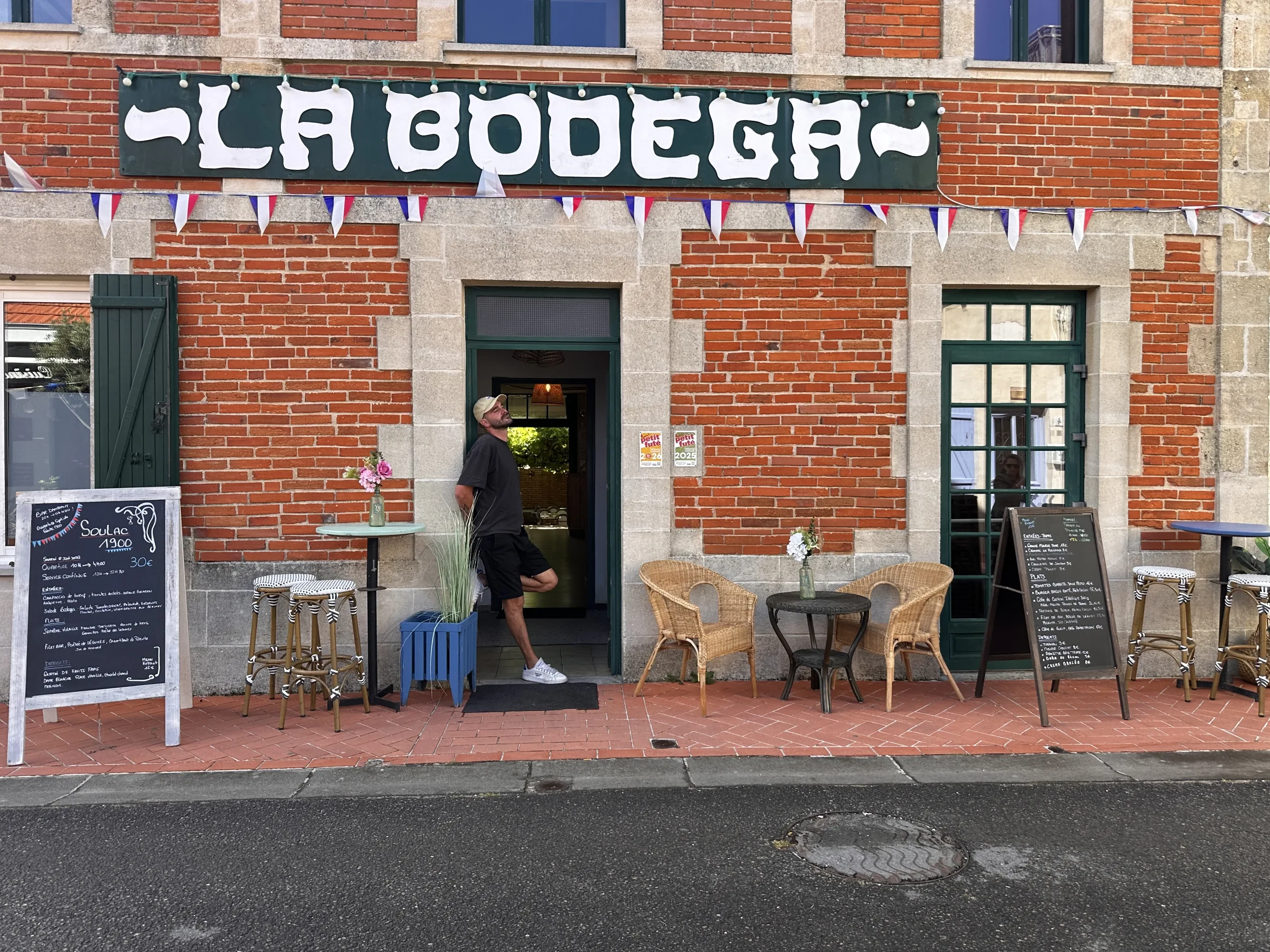 La façade en brique rouge de La Bodega — enseigne 'La Bodega' au-dessus de la porte verte