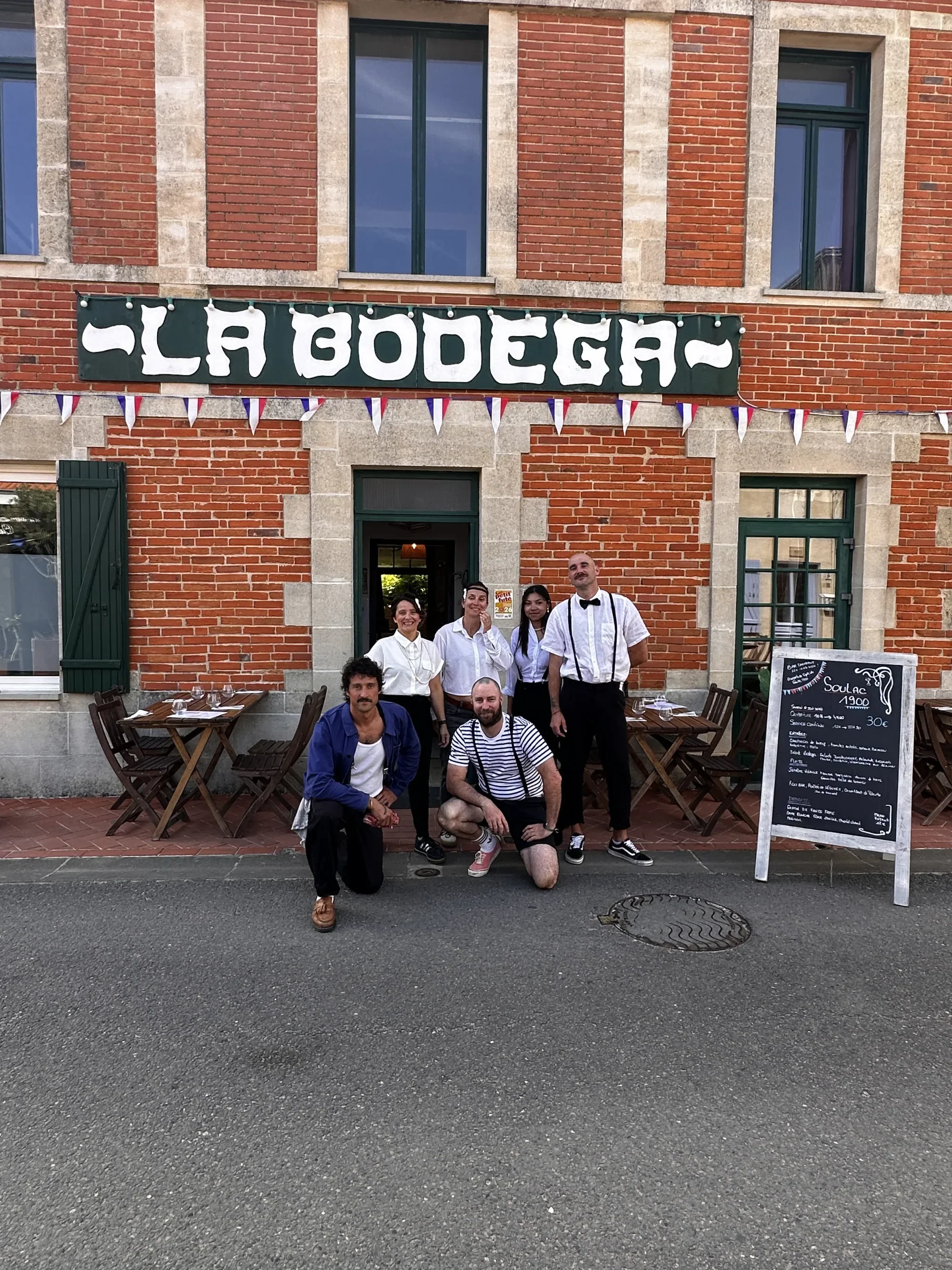 L'équipe de La Bodega devant la façade en brique rouge, sous les fanions tricolores