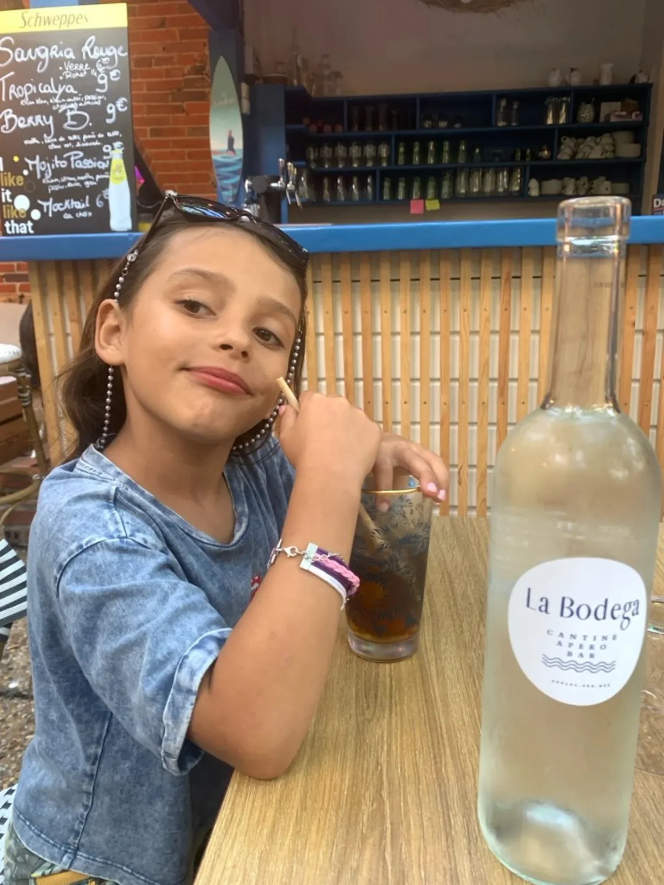 Une enfant dégustant un mocktail au comptoir, bouteille La Bodega à côté